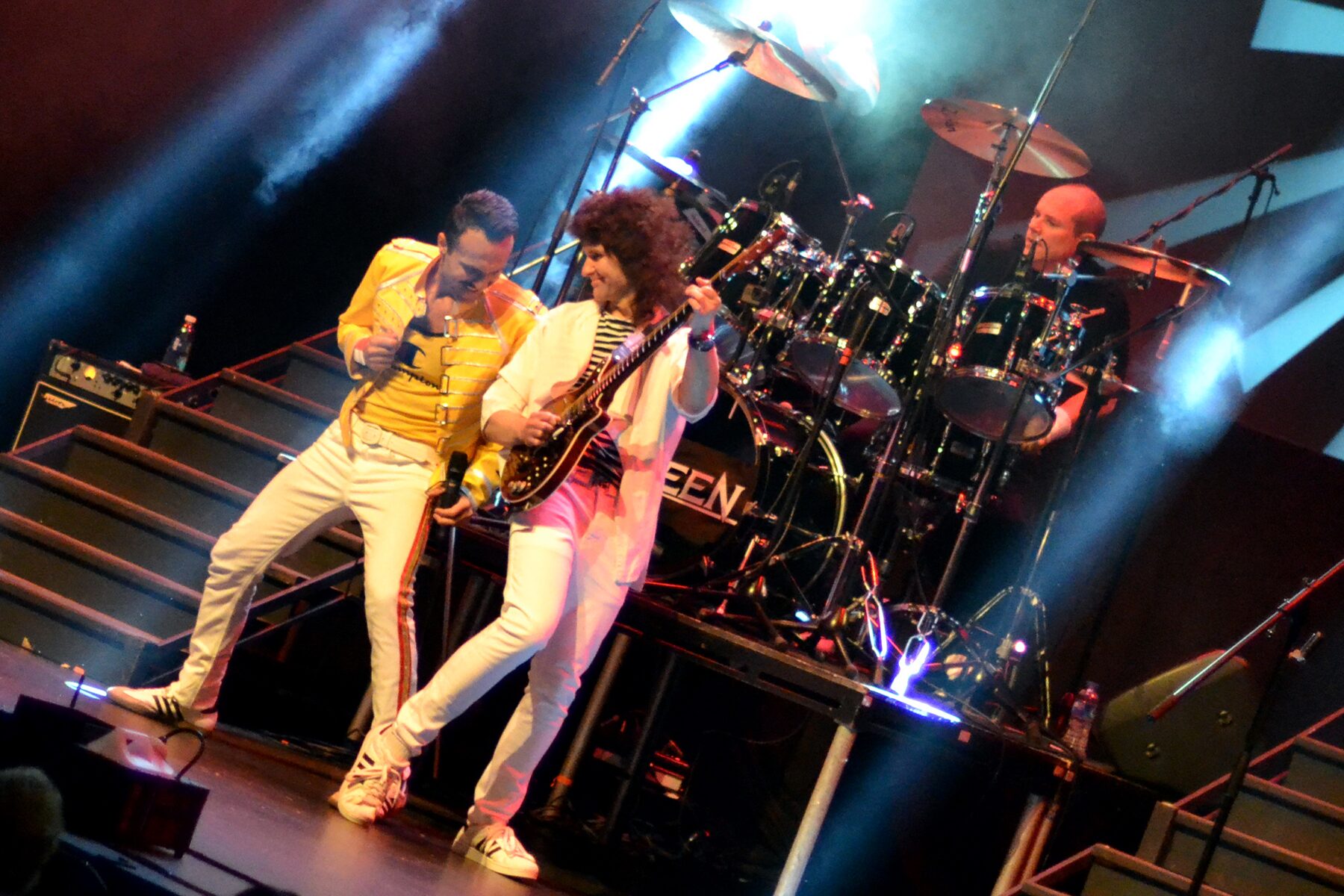 Flash Queen tribute band performing with Freddie Mercury in yellow jacket and Brian May on guitar