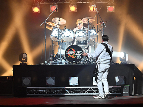 Mercury Queen tribute drummer and Freddie Mercury performer on stage with orange spotlighting